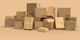 Tumpukan kotak karton polos berwarna coklat berbagai ukuran sebagai jenis box packaging. Kotak-kotak tersebut ditumpuk dengan rapi di atas palet kayu.